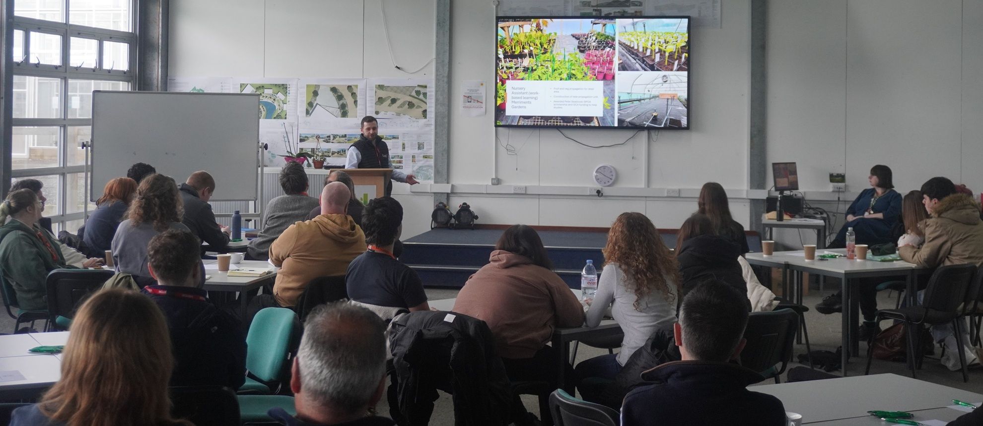 Person talking in front of presentation screen with crowd watching