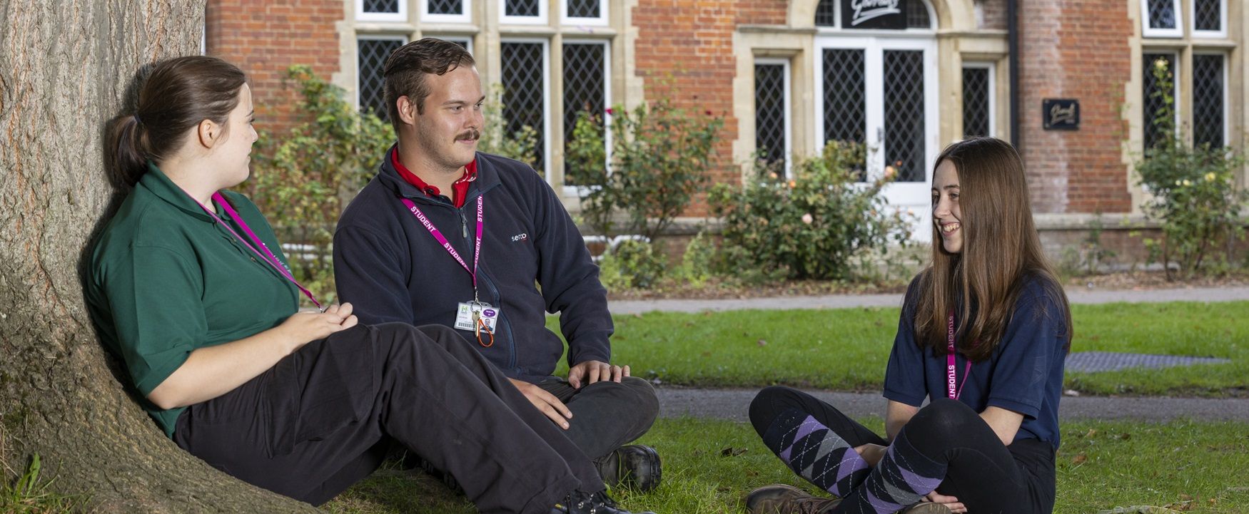 Three talking, sat outside next to tree