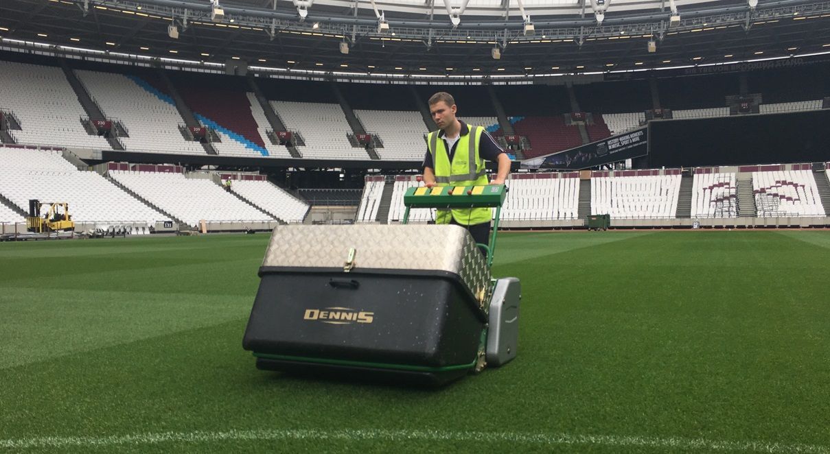 Young man pushing large lawnmower on football pitch